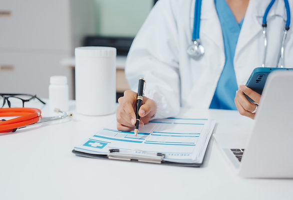 A doctor in a white coat with a stethoscope writes on a clipboard while holding a smartphone