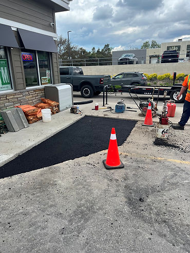 Fresh asphalt patch repair outside a commercial building with paving equipment