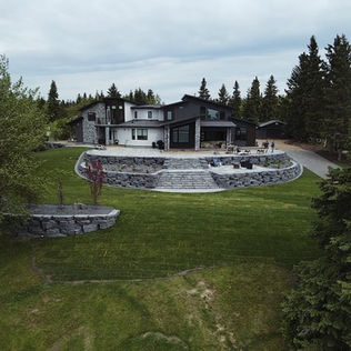 A large house featuring a stone wall and a well-maintained lawn
