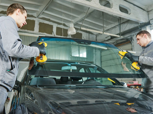 Two people installing a new windshield on a car.