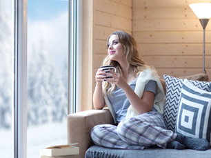 Cozy living room with a woman relaxing beside a large window overlooking a winter landscape.