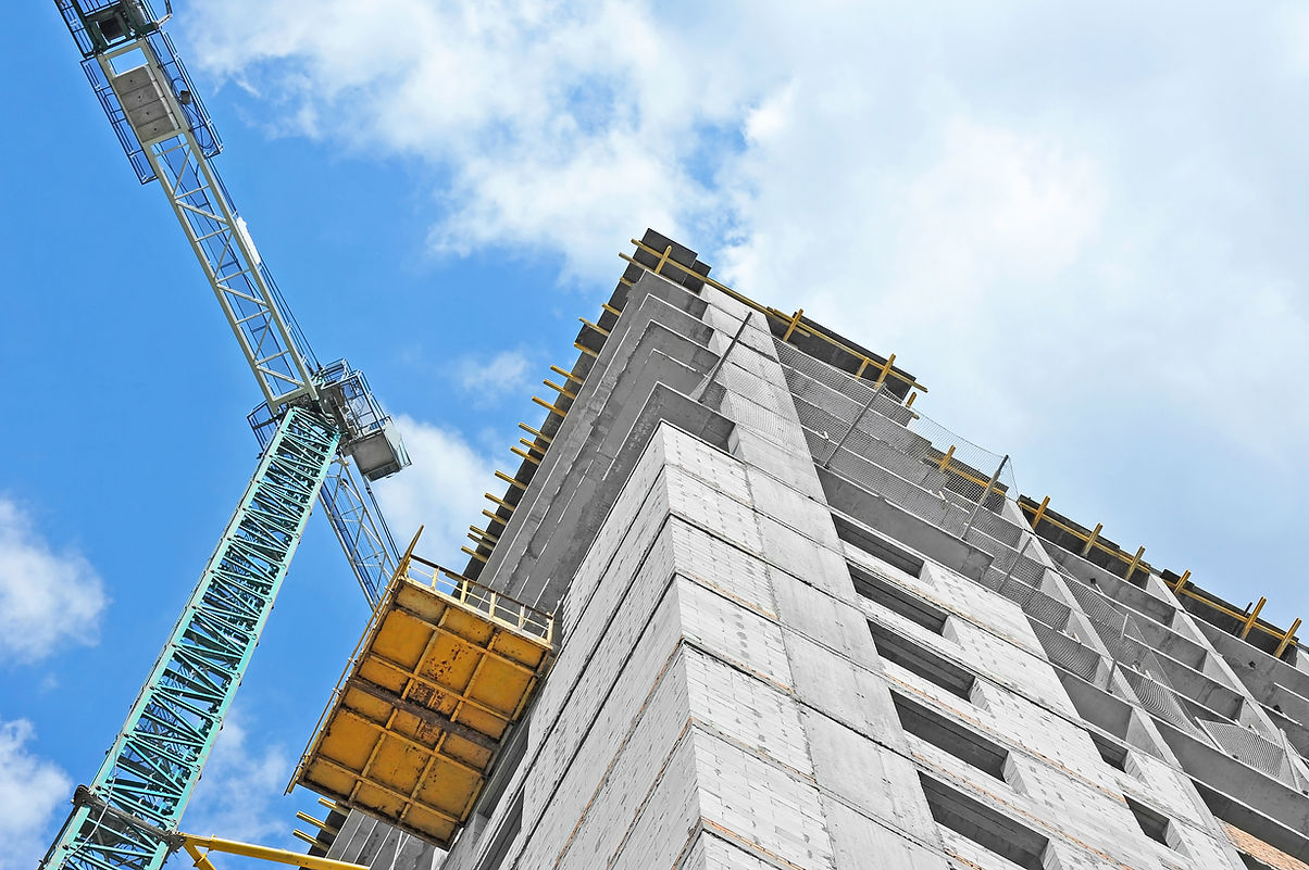 View from below of a modern grey building under construction, with a towering crane positioned alongside.