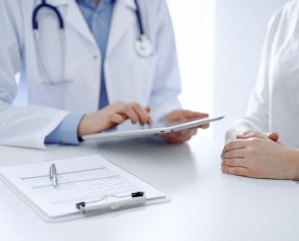 A doctor with a stethoscope holds a tablet, discussing with a patient