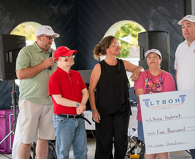 A diverse group of individuals gathered around a large check, engaged in conversation and celebration.