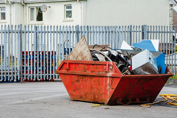 Large red metal roll-off dumpster filled with construction debris and junk