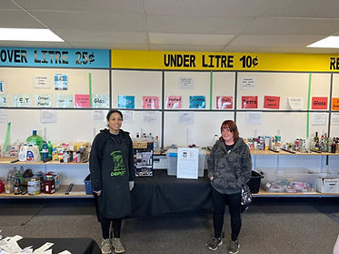 Two women stand beside a table displaying a sign