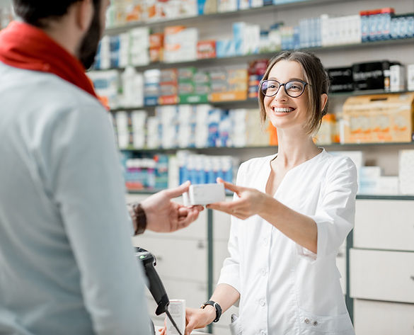 Smiling pharmacist in a white coat hands a medicine box to a male customer in a pharmacy