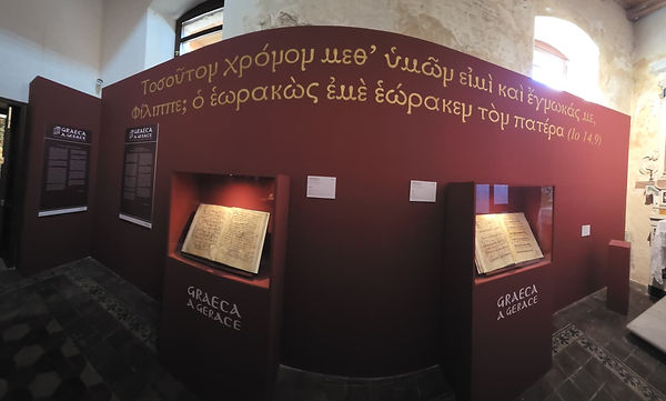 Exhibition display titled “Graeca a Gerace,” featuring illuminated medieval manuscripts in glass cases beneath a large inscription in Greek, celebrating Gerace’s enduring Greek and Byzantine heritage.