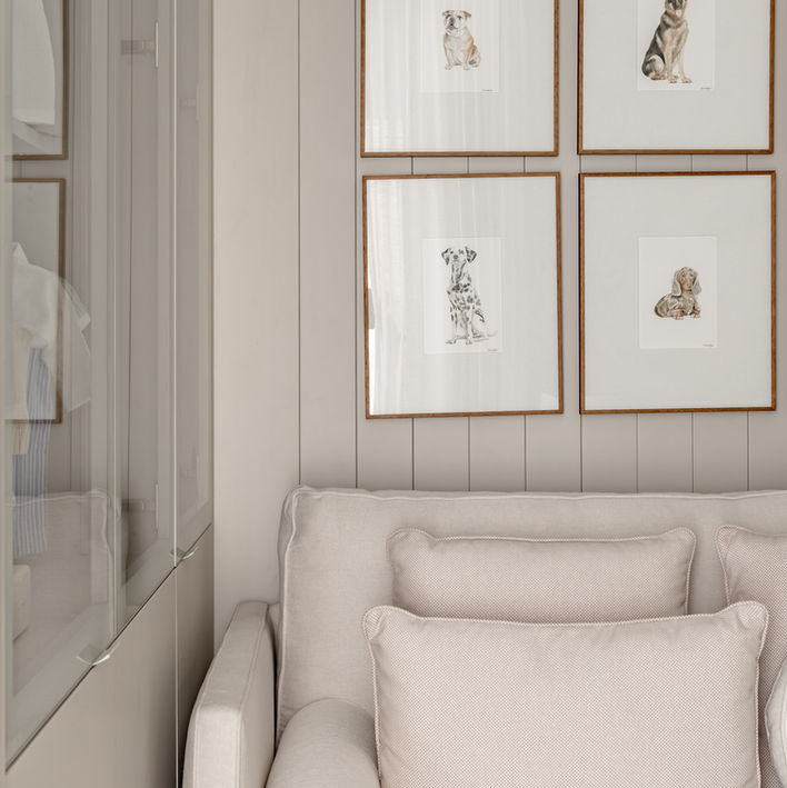 Quatro quadros com desenhos emoldurados sobre sofá bege claro em ambiente neutro.