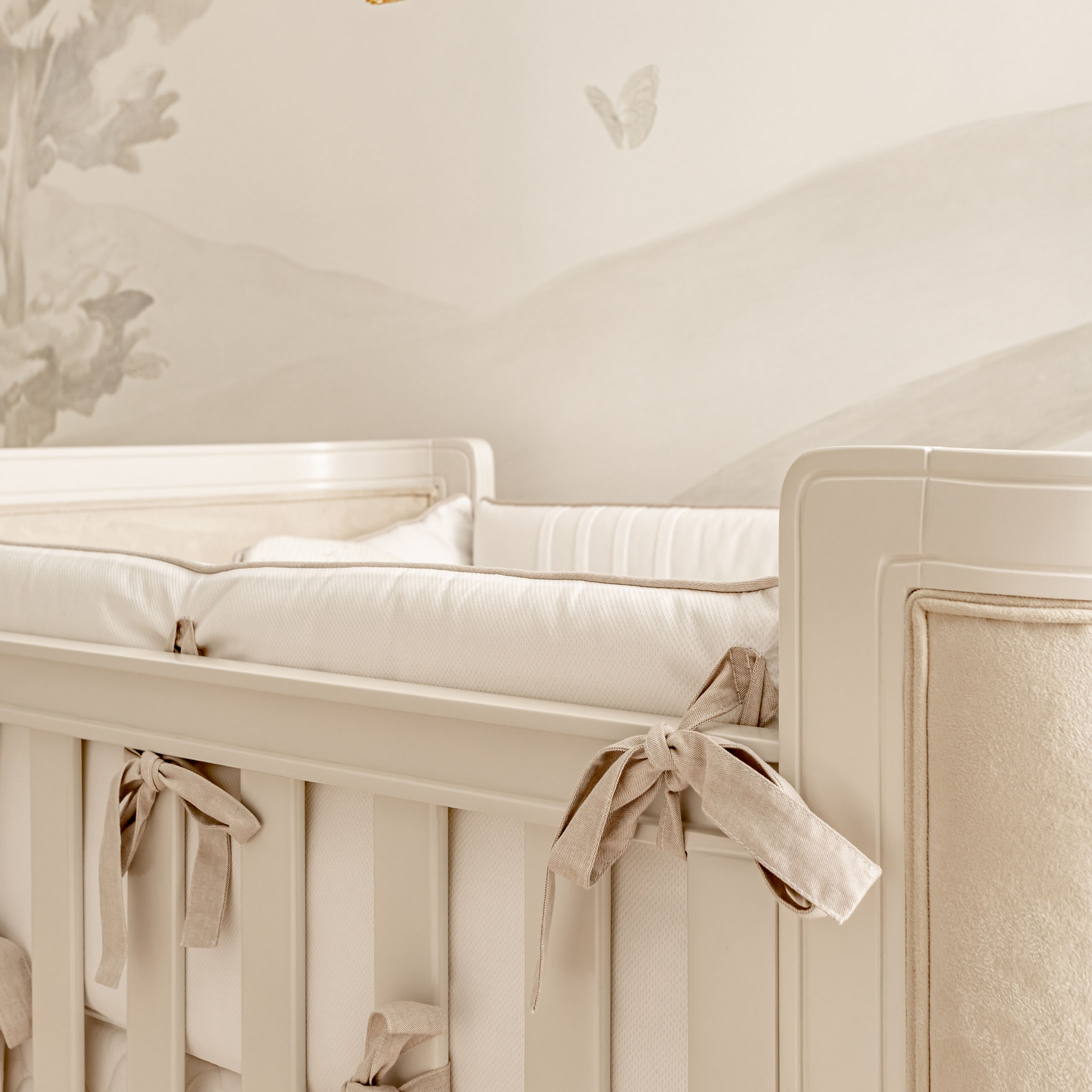Berço de bebê branco, detalhe de laços, fundo com detalhes em bege.