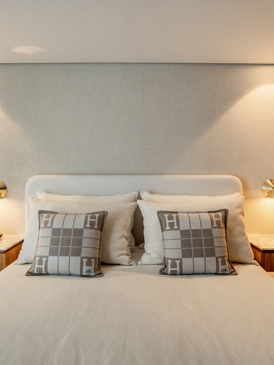 Quarto moderno com cama, travesseiros e abajures em um ambiente claro.