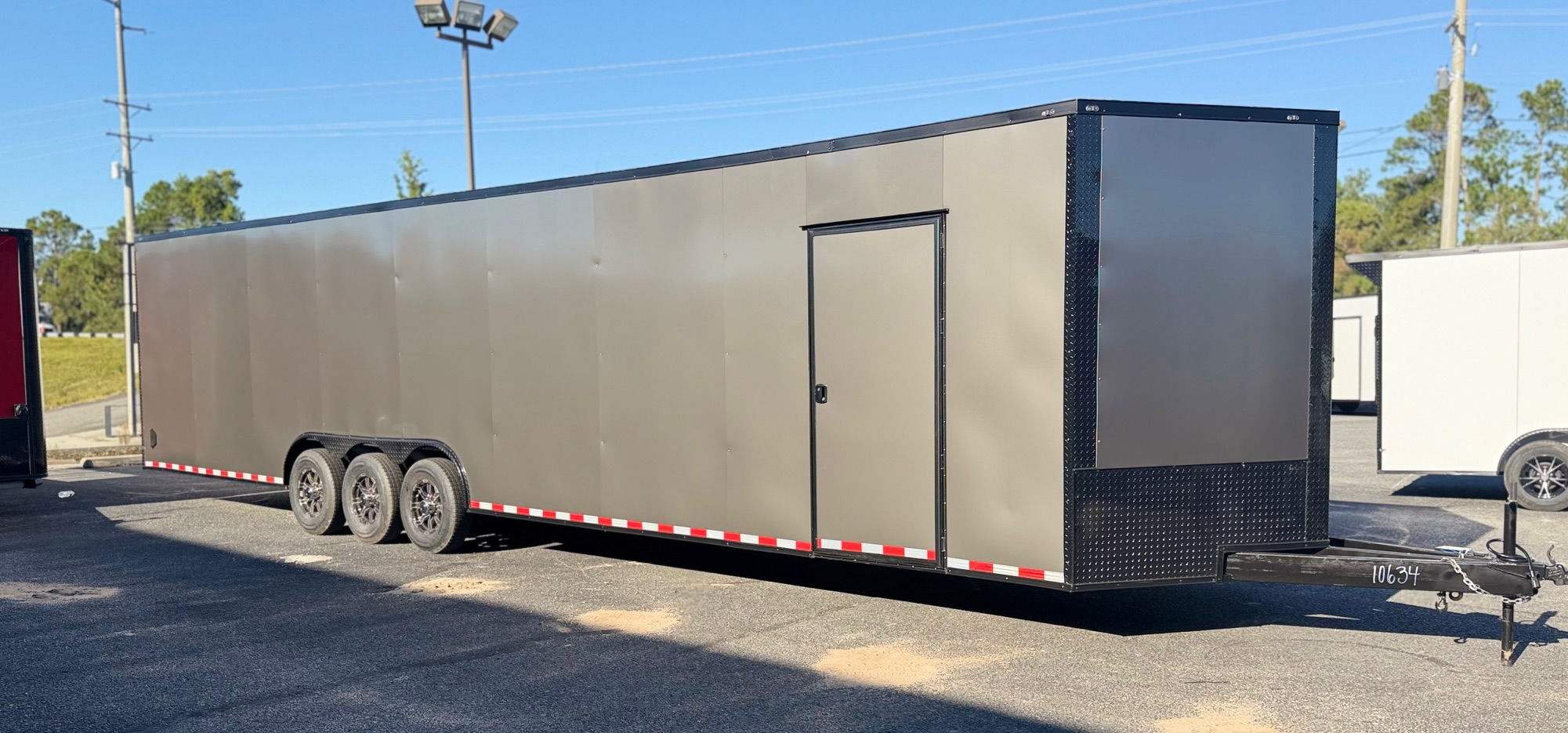Charcoal gray Deep South 8.5x36 triple axle enclosed car hauler trailer with blackout package, escape door, alloy wheels, extended tongue, and floor E-Track.
