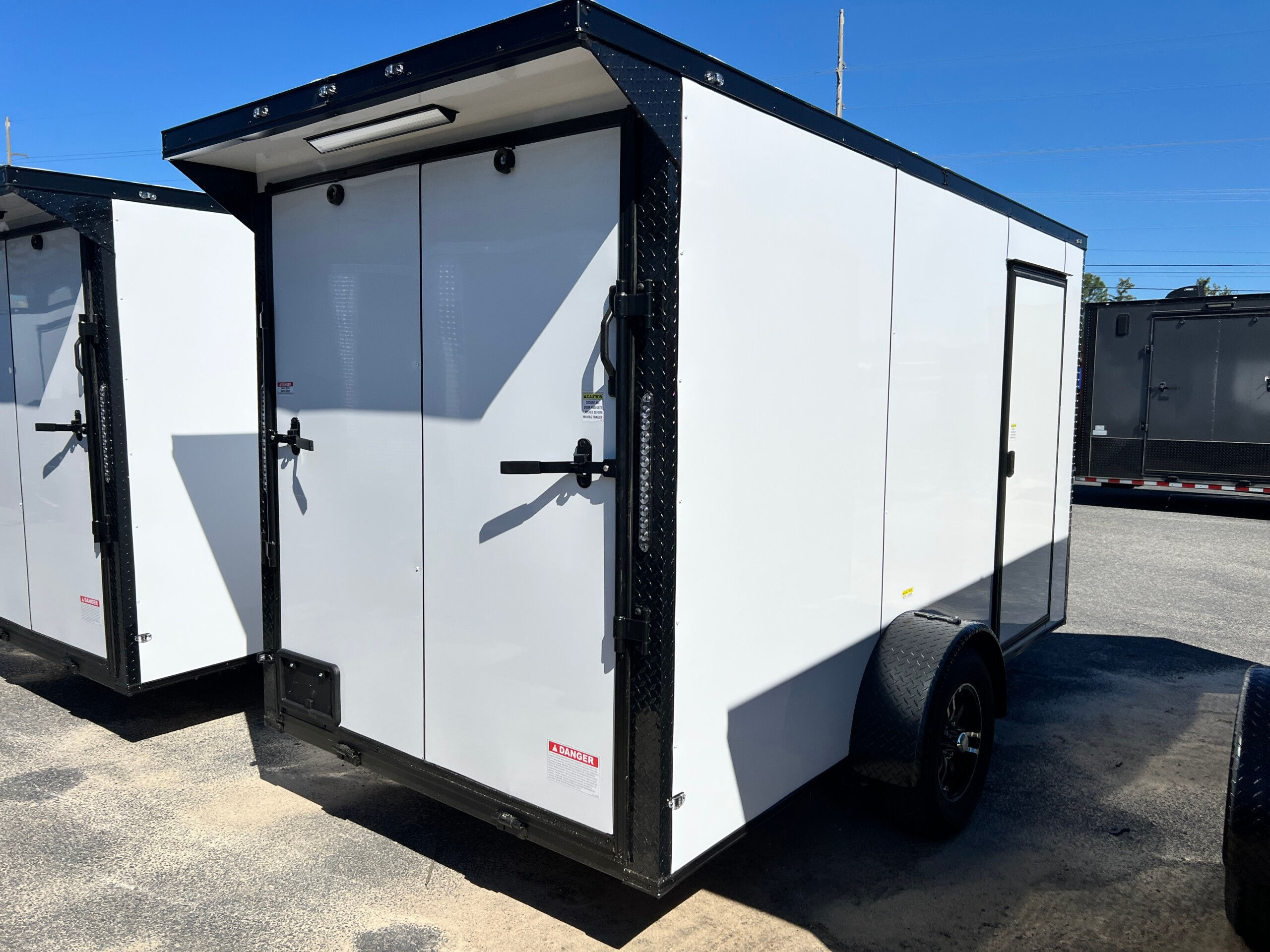 Deep South 6x12 white enclosed cargo trailer with Polycore exterior, blackout package, alloy wheels, spoiler, and ramp door.