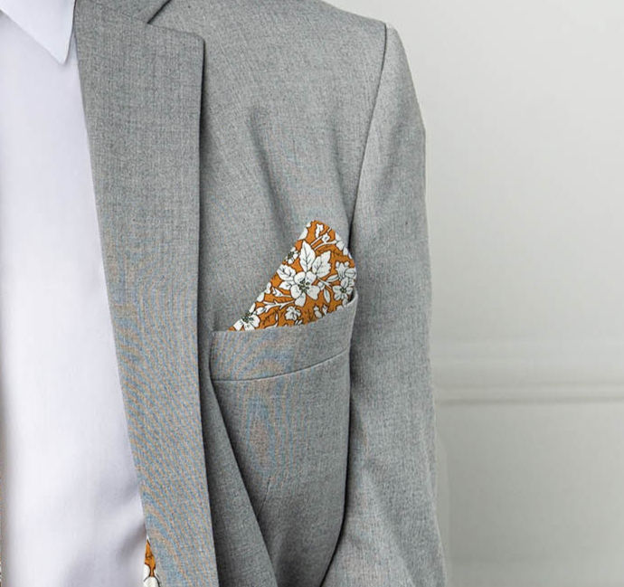 Burnt Orange Floral Pocket square on a grey suit jacket on a male model white background indoor