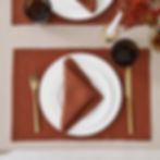 Burnt orange linen placemats styled on a wooden dining table with neutral plates and elegant table setting.