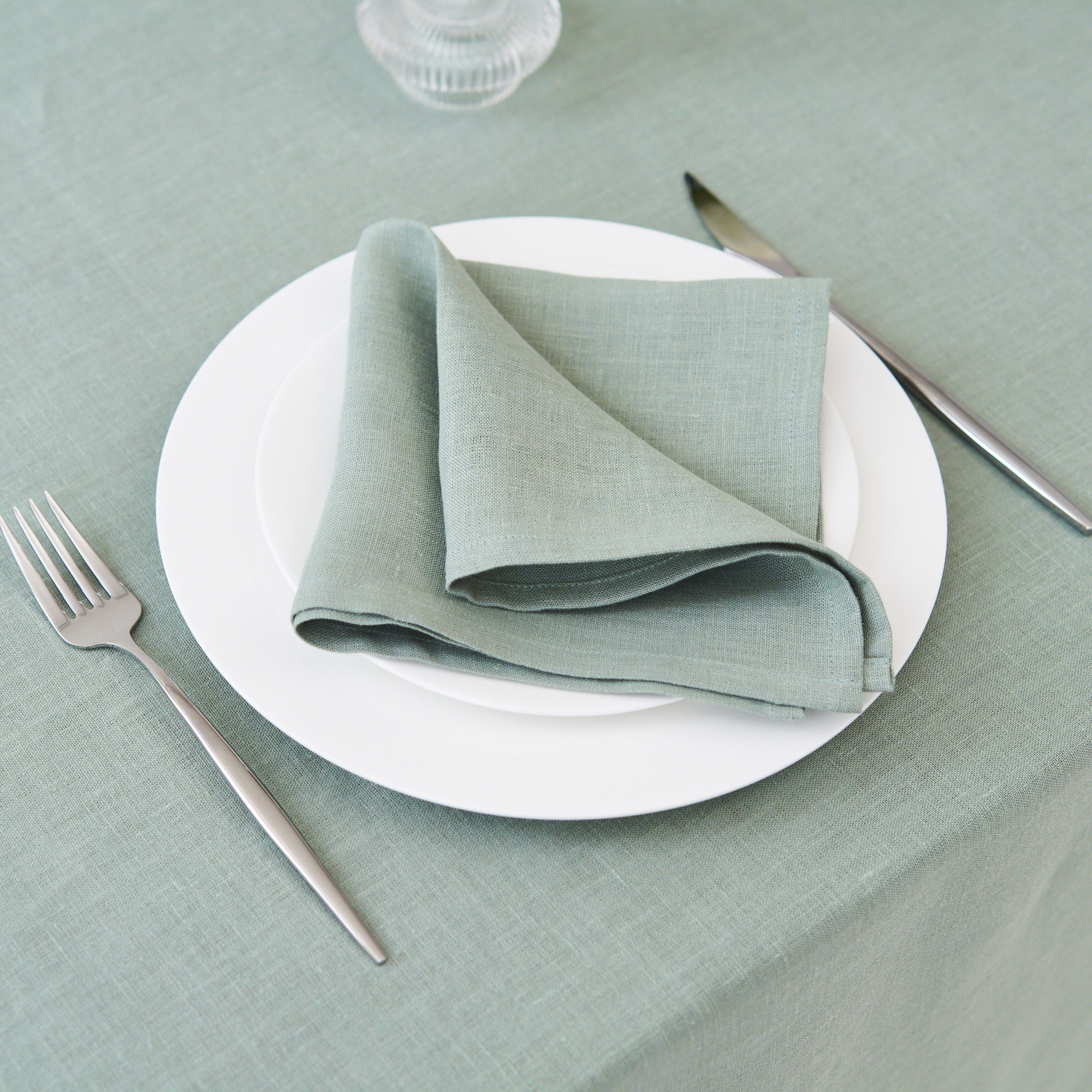 Light sage green linen napkin folded on a white plate with gold cutlery.