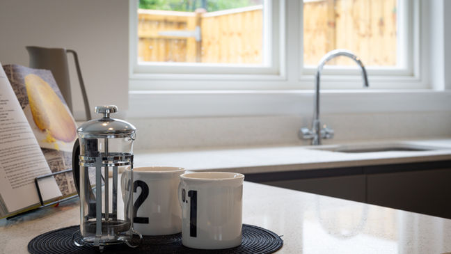 Coffee press and mugs beside a kitchen window