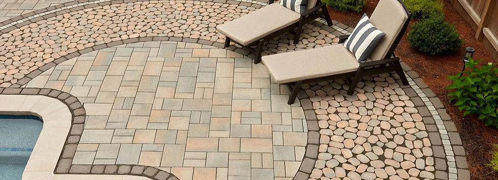 Patio with stone tiles featuring two beige lounge chairs with striped cushions beside a pool. Greenery borders the peaceful setting.