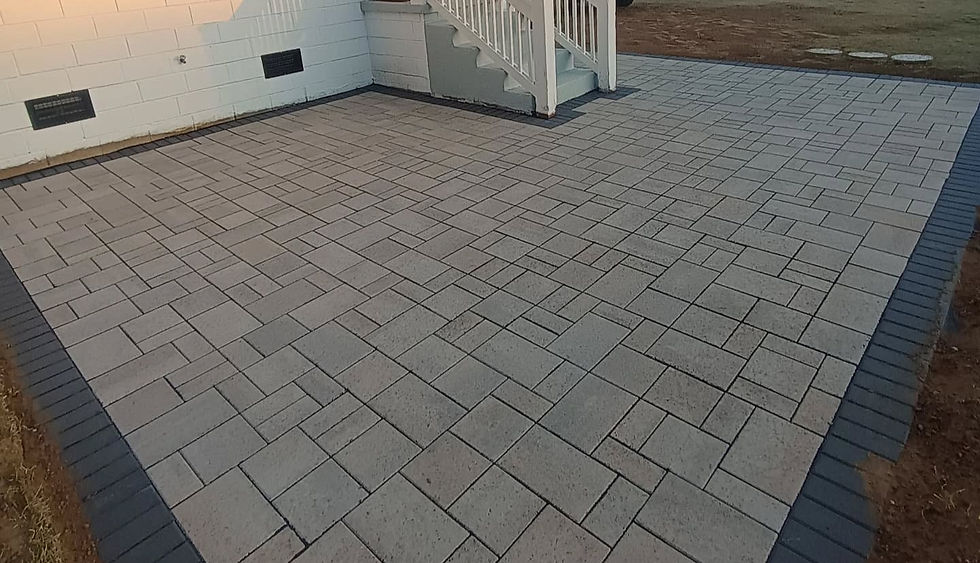 Brick patio with light gray pavers bordered by darker bricks. White steps lead to a building's entrance. Evening light casts a warm glow.
