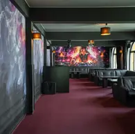 Lounge cu canapele din piele neagra, mocheta visinie si mural cu DJ