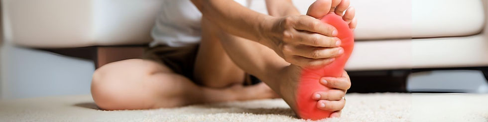 Person sitting on carpet, holding their red-colored sole, possibly indicating pain. Background features a blurred sofa, conveying a home setting.