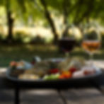 Cheese platter with bread, fruits, and meat on a picnic table. Two glasses of wine nearby. Wine tasting Fleurieu Peninsula package with platter at Magpie Springs for relaxed fun wine experience