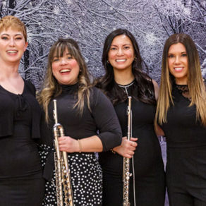 BETA Flute Quartet, standing side by side in front of a winter background, smiling while holding their instruments.