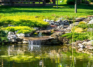 A waterfall and a pond in a grassy green park