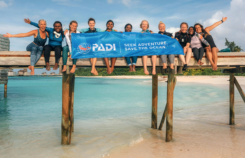 A group of delighted divers hold up the PADI Seek adventure Save the Ocean banner