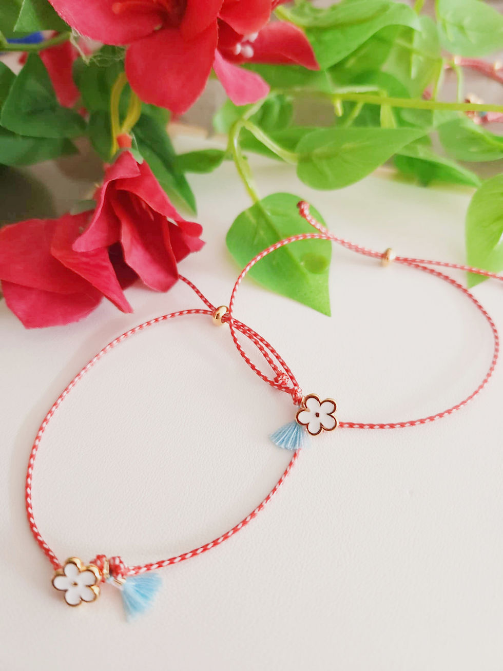 Two delicate red string bracelets with flower charms