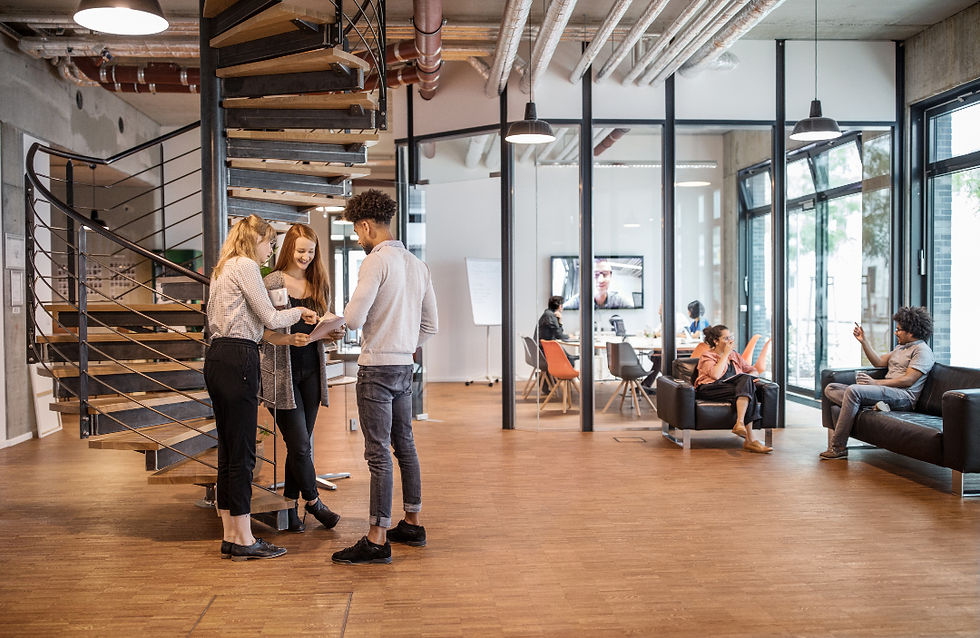 People collaborate by a spiral staircase in a modern office with glass walls and wooden floors. Relaxed mood, screens visible in the background. Demonstrating EIC Accelerator