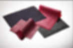 Various textured fabrics: black with circles, red with a snake pattern, pink with a grid, and dotted black, layered on a white background.
