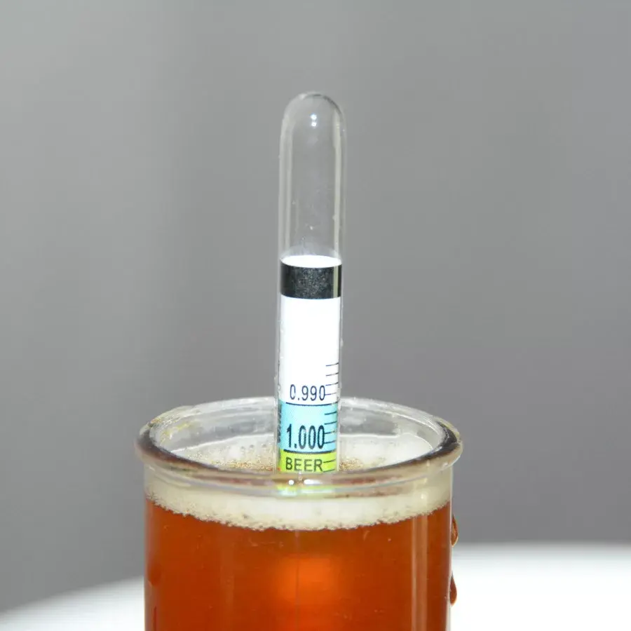 Hydrometer floating in a glass of beer, displaying the specific gravity for alcohol measurement