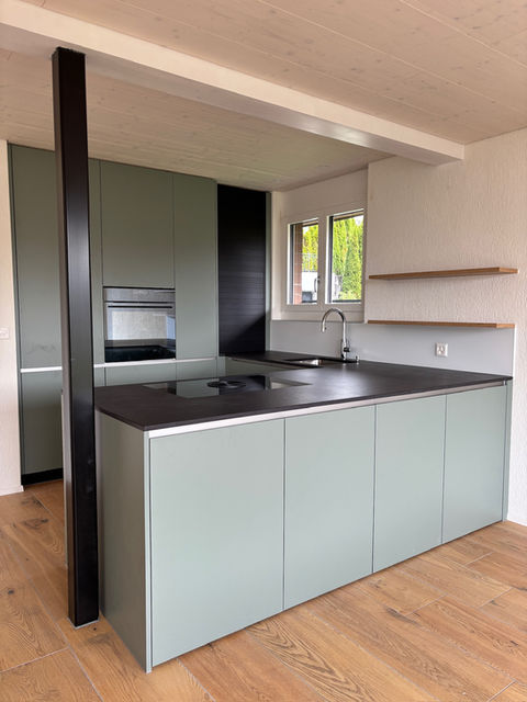 Grüne Küche mit Edelstahlgriffen und schwarzer Granitarbeitsplatte in 5607 Möriken-Wildegg. Modernes Design mit einem eleganten Kontrast zwischen Grün und Schwarz.