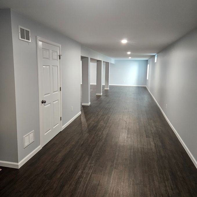 Completed basement remodel featuring luxury vinyl plank flooring, recessed lighting, painted support columns, and a spacious open-concept layout by HS Premier Construction Services.