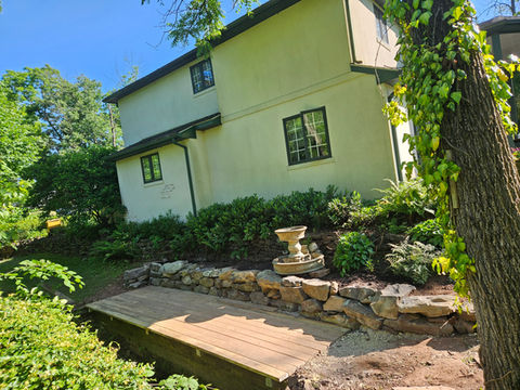 Custom wooden garden walkway constructed by HS Premier Construction Services with natural timber decking, stone retaining walls, and landscaped surroundings.
