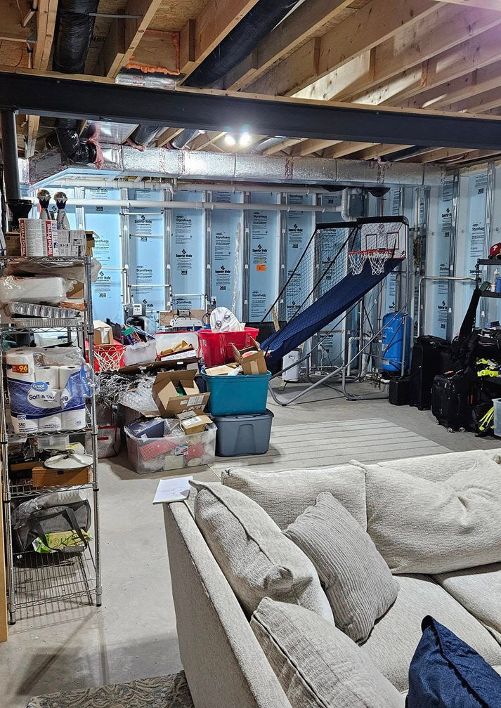 Original unfinished basement showing exposed framing, insulation, storage space, and unfinished concrete floors before remodeling.