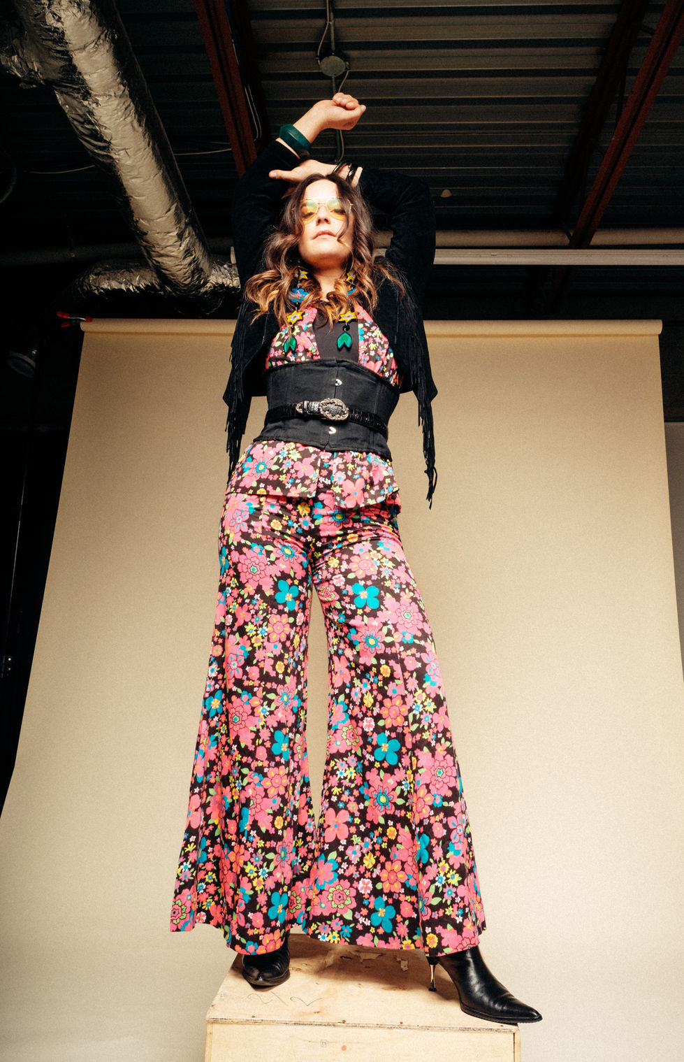 a woman wearing a black fringed jacket and floral pants