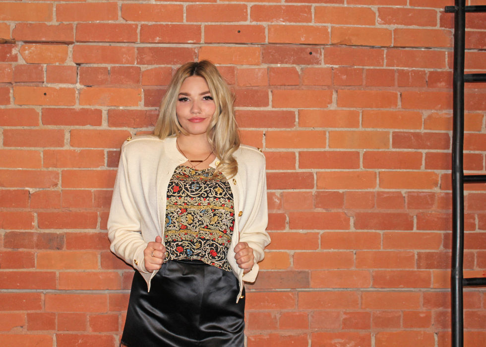 a woman wearing a white jacket and a black skirt stands in front of a brick wall