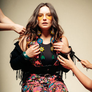 a woman wearing sunglasses and a floral vest is surrounded by people
