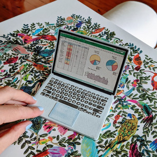 A pale human hand is using a miniature painted paper laptop