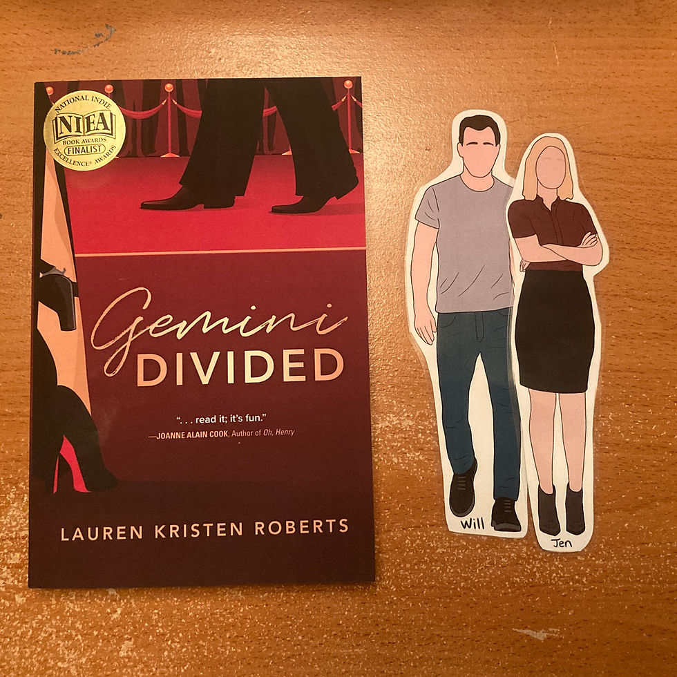 One copy of the book called Gemini Divided beside two bookmarks shaped like the main characters, Jen and Will. Jen is in a button down short sleeved blouse and a skirt, and Will is in jeans and a t-shirt.