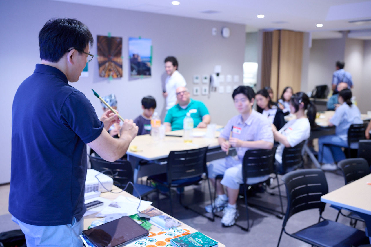 文化ワークショップで、男性がアイルランドの伝統楽器「ティンホイッスル」の演奏方法を子どもや大人に実演している様子。