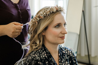 Die Braut bekommt den Haarkranz aus zarten Trockenblumen während des Getting Ready ins Haar gebunden.