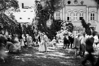 Kreatives Hochzeitsgruppenfoto: Brautpaar küsst sich vor dem historischen Gutshaus des KulturGut Wrechen, während die Gäste in Bewegungsunschärfe verschwimmen und eine besondere Dynamik erzeugen.