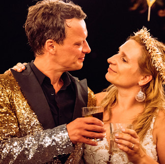 Das Brautpaar prostet sich vor dem dunklen Nachthimmel zu: Der Bräutigam im funkelnden Partyanzug und die Braut mit glitzernden Party-Ohrringen – ein funkelnder Moment voller Freude.