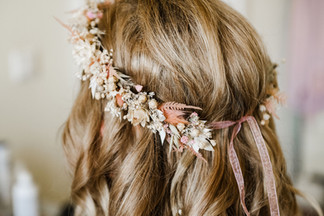 Der fertig gebundene Haarkranz in zarten Pastell- und Rosatönen auf dem blonden, gewelltem Haar der Braut beim Getting Ready.