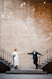 Cooles Paarfoto beim Brautpaarshooting: Das Brautpaar steht jeweils auf einer Treppe und reicht sich die Hände, was an den Beginn einer romantischen Tanzszene erinnert – aufgenommen von Spreekind-Fotografie, Hochzeitsfotografin Berlin.