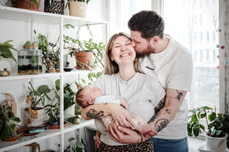 Familienmoment mit Neugeborenem, Papa schenkt Mama ein zärtliches Küsschen