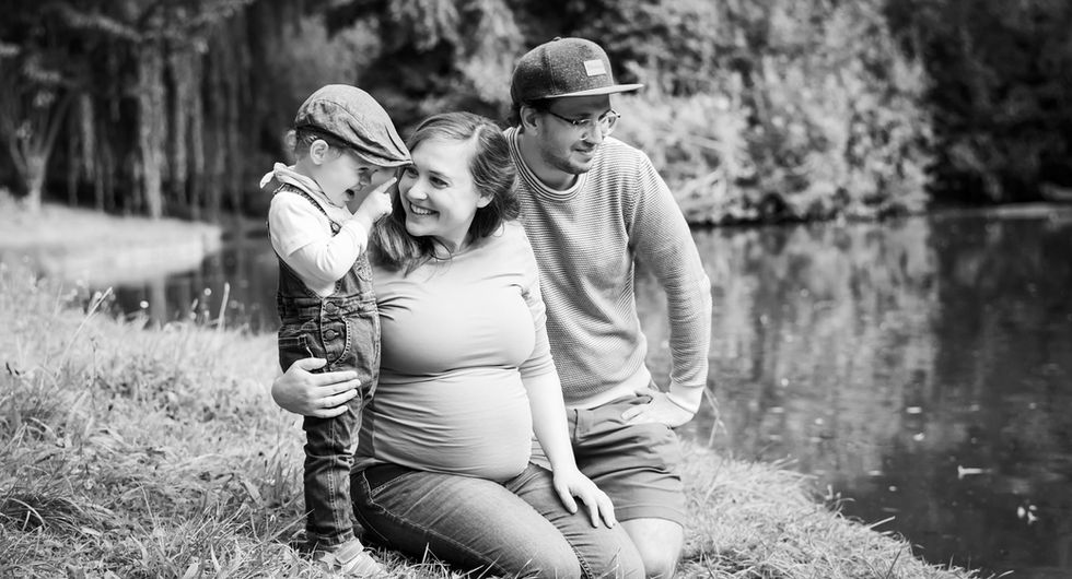 Babybauch Shooting in der Natur mit Partner und Kleinkind, ein natürlicher Familienmoment voller Liebe und Emotionen.